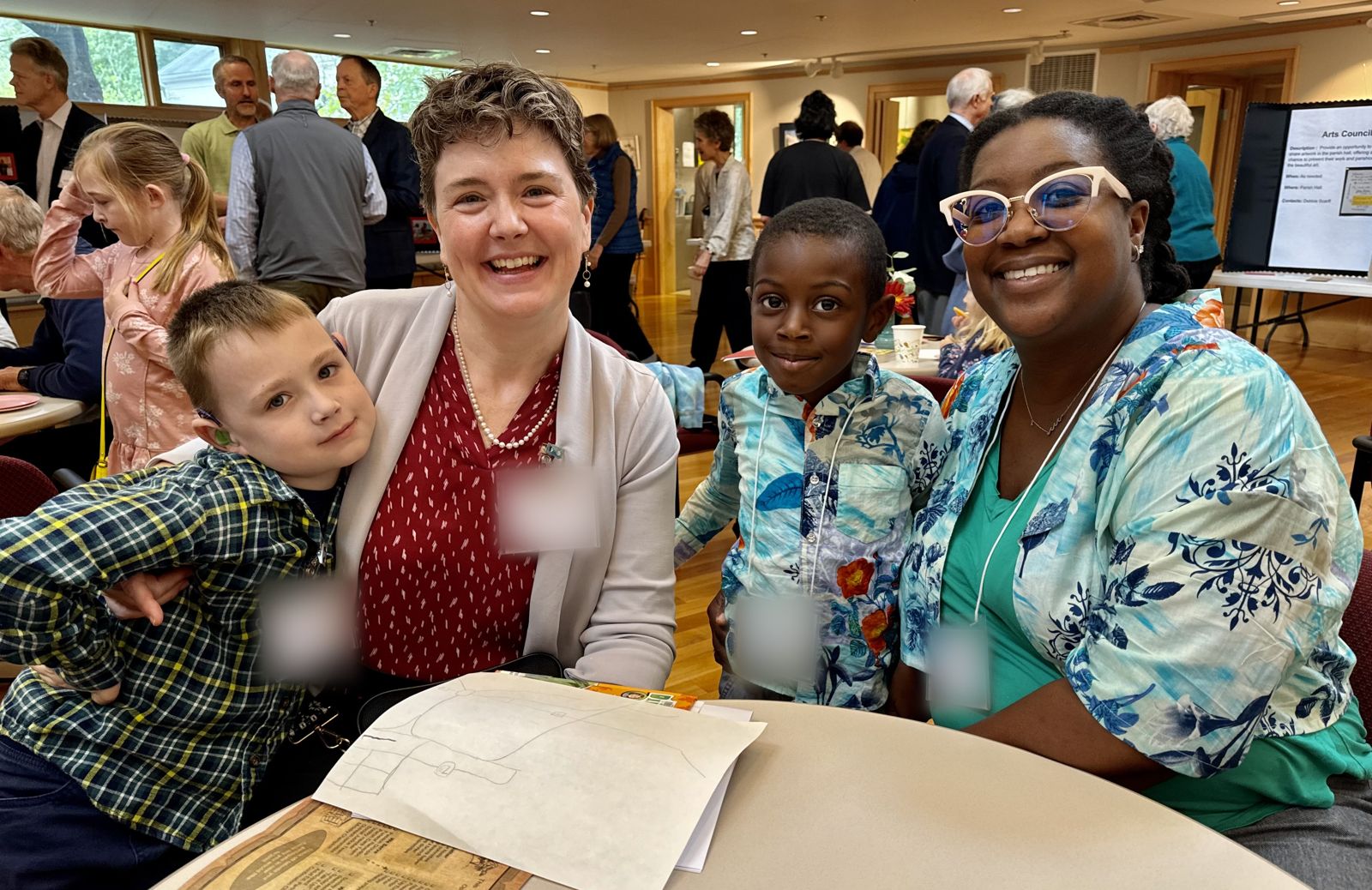 Two smiling parents with their young sons at a table during coffee hour in the parish hall